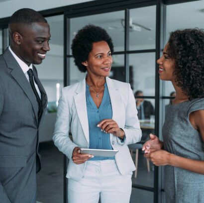 Shot of three coworkers having a discussion in modern office. Successful business team in meeting using digital tablet and discussing business strategy. Confident business people working together in the office. Corporate business persons discussing new project and sharing ideas in the workplace.